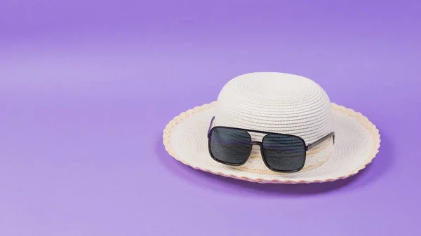 Wiklinowy kapelusz i okulary przeciwsłoneczne na liliowym tle. — Zdjęcie stockowe
