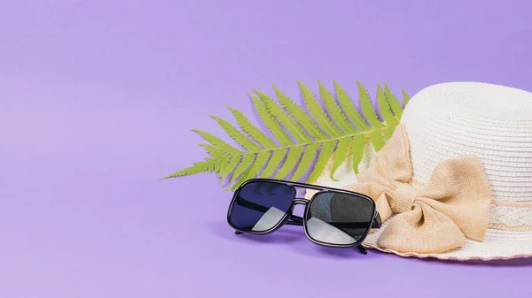 Kompozycja okularów przeciwsłonecznych, kapelusza i liścia palmy na fioletowym tle. — Zdjęcie stockowe