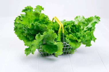 Beyaz ahşap bir masanın üzerinde bir sürü marul yaprağı olan bir yemek sepeti..