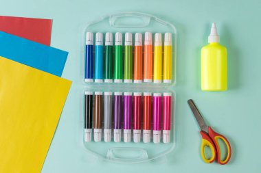 Açık arkaplanda makas, yapıştırıcı, işaret ve renkli kağıt.