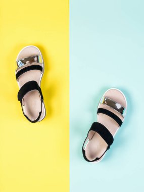 Sarı ve mavi arka planda siyah kadın sandaletleri. Düz yatıyordu.