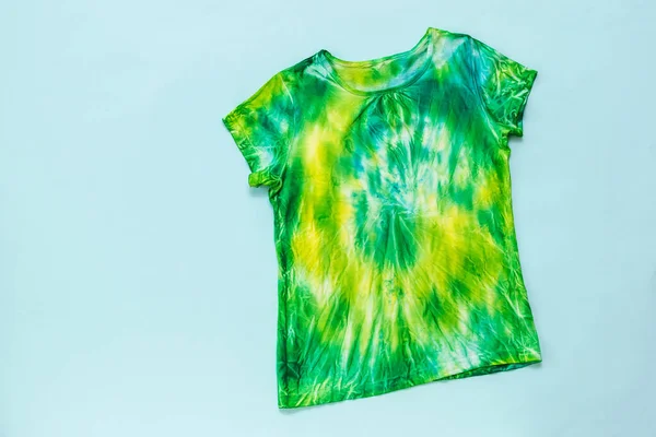 T-shirt em verde, amarelo e azul em estilo tie dye em um fundo azul claro. Depósito plano . — Fotografia de Stock