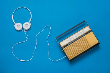 Üzerinde dinleme cihazı ve mavi arka planda retro radyo olan beyaz kulaklıklar. Klasik teknik.