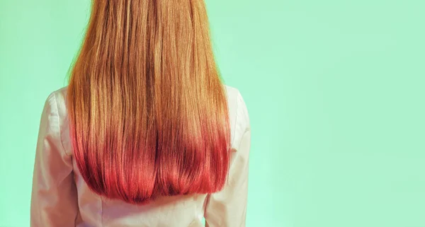 Uma menina com cabelos parcialmente coloridos em rosa em um fundo verde claro . — Fotografia de Stock