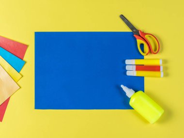 Sarı arka planda renkli kağıt, makas, yapıştırıcı ve işaretleyiciler.