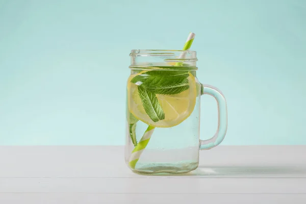 Água fria com limão e hortelã em uma xícara de vidro em uma mesa branca . — Fotografia de Stock