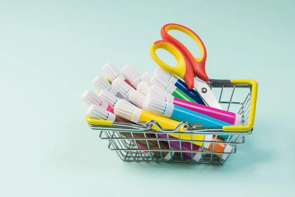 Colored markers and scissors in the basket on a light background.