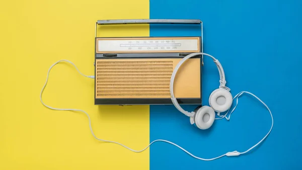 Auriculares blancos conectados a una radio antigua sobre un fondo amarillo y azul. Técnica vintage . — Foto de Stock