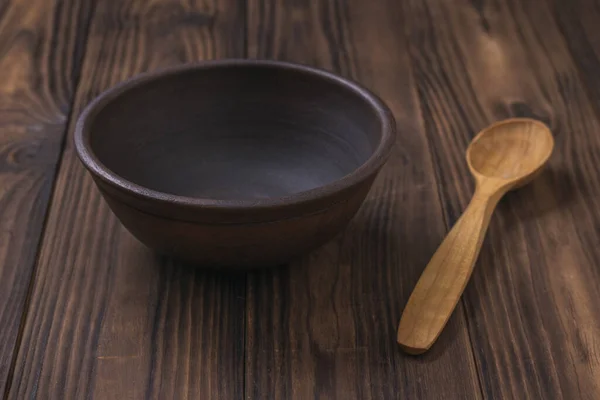 Una cuchara de madera ligera y un tazón de barro sobre una mesa de madera . — Foto de Stock