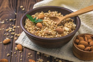 Tahta bir masada, kil bir kupadaki bademlerle granola..