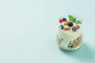 Büyük bardakta granola, yoğurt ve açık mavi arkaplanda böğürtlen..