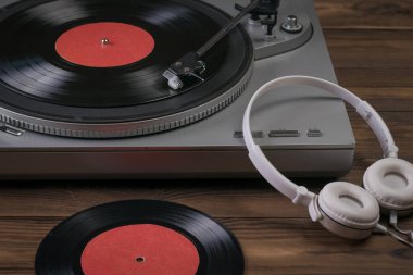 Plastik bir disk ve beyaz kulaklıklar ahşap bir masada oynatıcının yanındadır..