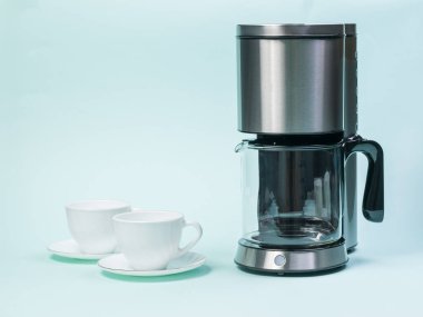 Damlayan bir kahve makinesi ve mavi arka planda iki beyaz bardak..