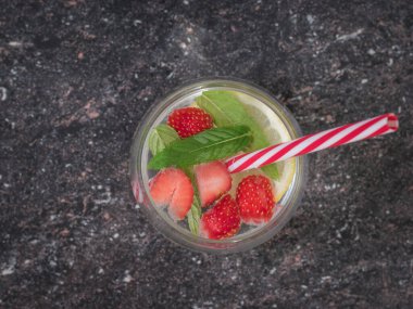 Taş zeminde bir bardak soğuk su ve böğürtlen manzarası.