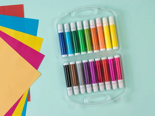 Un conjunto de marcadores y un conjunto de hojas de papel de color sobre un fondo azul claro . —  Fotos de Stock