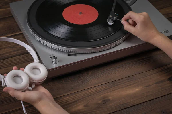 Ruce držící bílá sluchátka a umísťující na přehrávač vinylový disk. — Stock fotografie