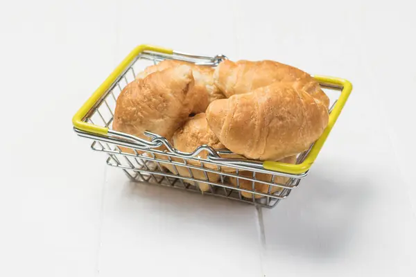 ตะกร้าโลหะที่มี croissants บนโต๊ะไม้สีขาว . — ภาพถ่ายสต็อก