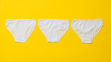 Parlak sarı arka planda üç beyaz kadın külotu. Düz yatıyordu.