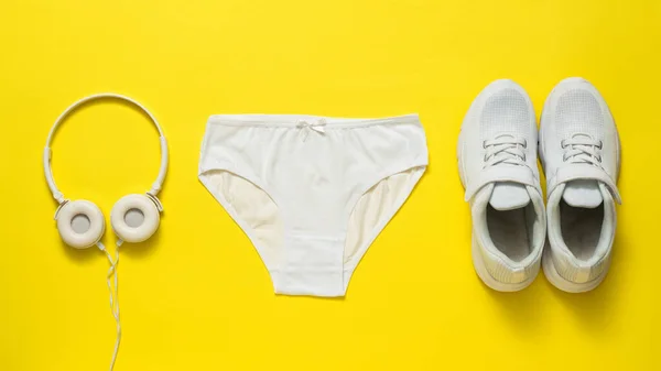 Mutandine bianche, scarpe da ginnastica e cuffie su sfondo giallo. — Foto Stock
