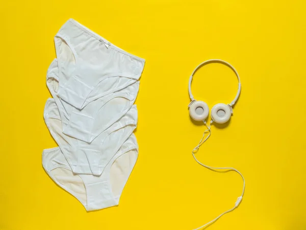 Una pila de calzoncillos blancos y auriculares blancos sobre un fondo amarillo. Ropa interior. La vista desde arriba. — Foto de Stock
