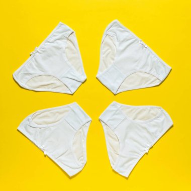 Parlak sarı arka planda dört beyaz kadın külotu. Düz yatıyordu.