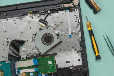 İşlemci soğutma vantilatörü ve sökülmüş dizüstü bilgisayar mavi arka planda.