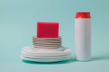 Temizlik tozu, kırmızı köpük sünger ve mavi arka planda temiz tabaklar..