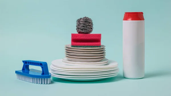 Dish brushes, cleaning powder and a set of white dishes on a blue background.