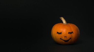 Siyah arka planda yüzü boyanmış bir balkabağı..