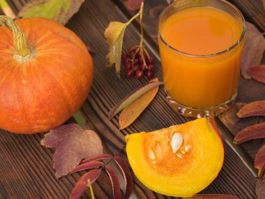 Bir bardak balkabağı suyu ve sonbahar yapraklı bir parça balkabağı..