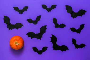 Mor bir arka planda olgun bir balkabağı ve yarasa sürüsü.