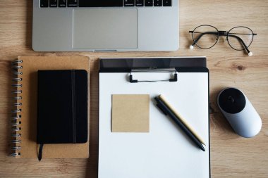 Not defterli ahşap masaüstü, kağıtlı klasör, kağıt, kalem, çıkartma, gözlük, fare ve takvimli dizüstü bilgisayar