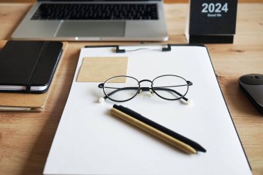 Not defterli ahşap masaüstü, kağıtlı klasör, kağıt, kalem, çıkartma, gözlük, fare ve takvimli dizüstü bilgisayar