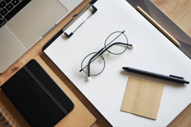Not defterli ahşap masaüstü, kağıtlı klasör, kağıt, kalem, çıkartma, gözlük, fare ve takvimli dizüstü bilgisayar