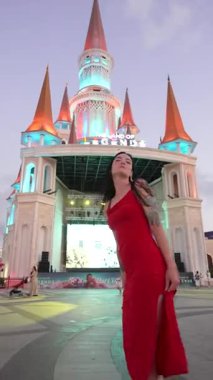 Kırmızı elbiseli kız bir şatonun arka planında poz veriyor.