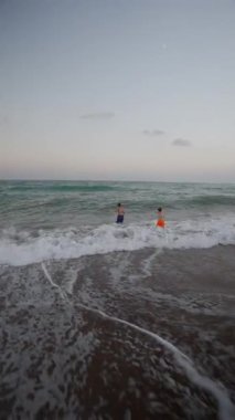 Çocuklar sahilde deniz dalgalarıyla oynuyorlar.