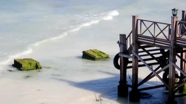 Deniz suyunun dokunduğu beyaz kumlu plajda ahşap köprü