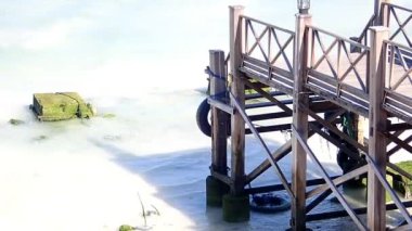 Deniz suyunun dokunduğu beyaz kumlu plajda ahşap köprü
