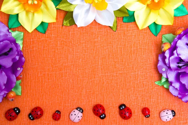 Rahmen aus hellen künstlichen Blumen und Marienkäfern - ein mehrfarbiger Hintergrund — Stockfoto