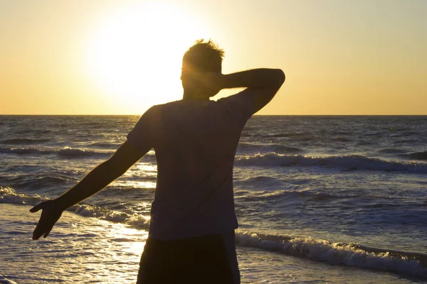 Молодой человек руки за голову расслабиться на восходе солнца море — стоковое фото