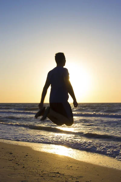 Genç adam gün doğumu mavi gökyüzü ve deniz, plaj atlamak