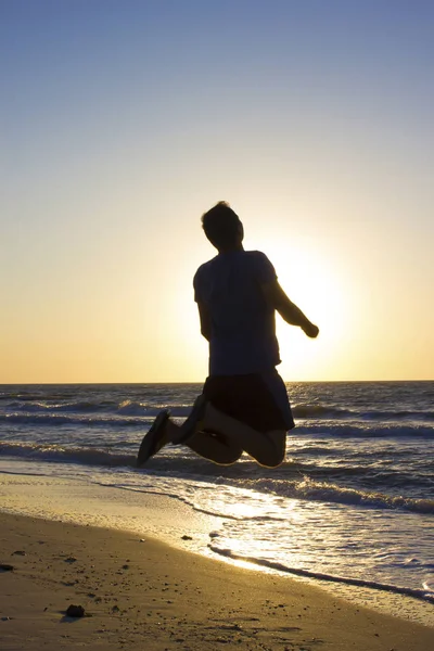 Genç adam gün doğumu mavi gökyüzü ve deniz, plaj atlamak