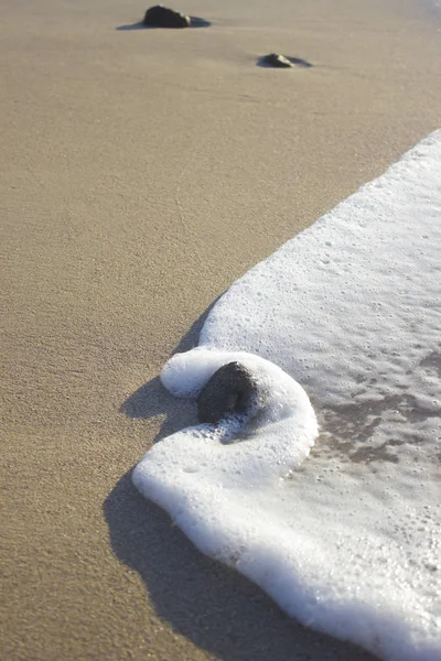 Piedra en espuma de olas de mar sobre arena amanecer mar — Foto de Stock