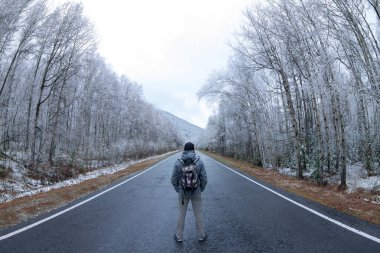 Gri adam karlı bir ormandaki gri yolun ortasına bir sırt çantası konumu olan.