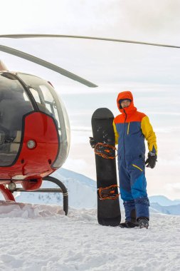 Snowboard freerider helikopter karlı dağlarda, kışın bulutlar altında duruyor.