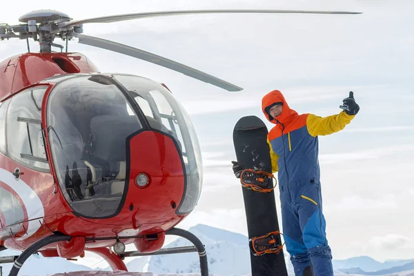 Snowboardåkare freerider står vid helikoptern i de snötäckta bergen i vinter under molnen — Stockfoto