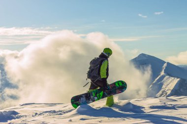 Snowboardcu Freerider kışın karlı dağlarda bulutların altında duruyor.