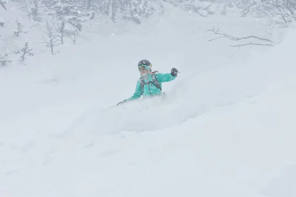 Kvinna snowboardåkare freerider går ner på pudersnö i bergen i ett snöfall — Stockfoto