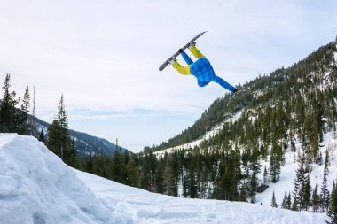 Snowboard freerider orman ve dağlar bir arka plan üzerinde bir kar rampa güneşin üzerinden atlama