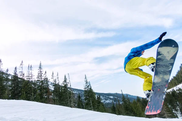 Snowboarder Freerider springt von einer Schneerampe in der Sonne vor dem Hintergrund von Wald und Bergen — Stockfoto
